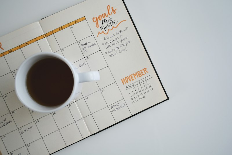 Agenda abierta con un calendario mensual, metas escritas a mano y una taza de café